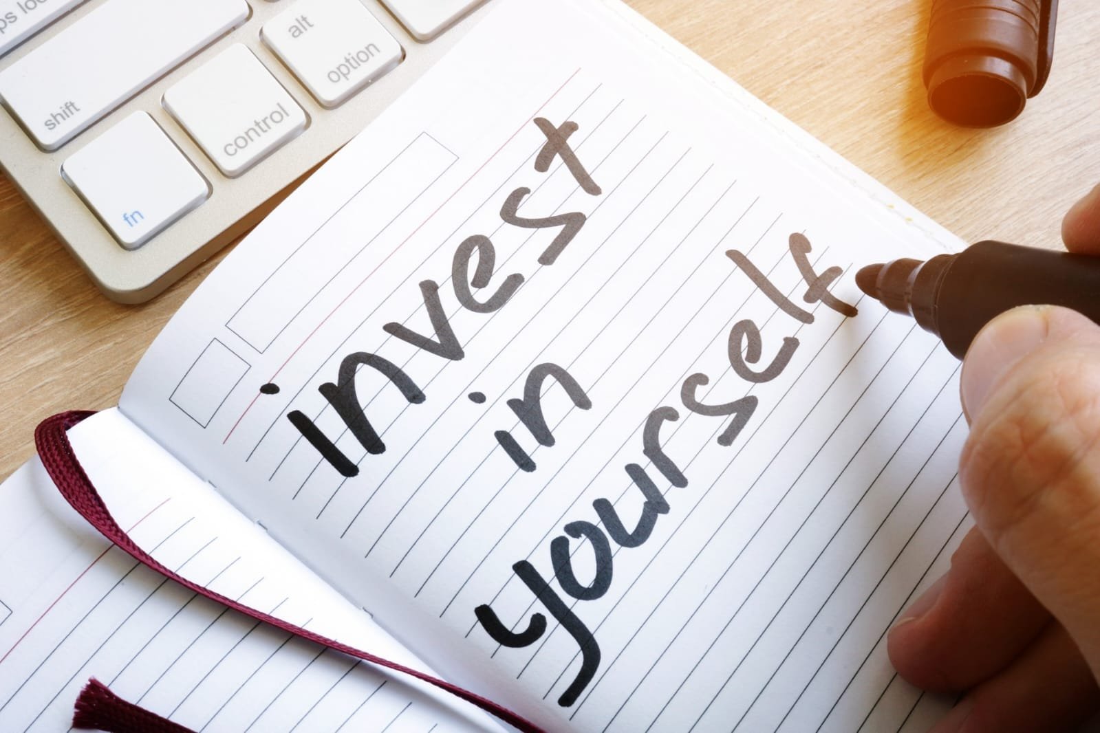 Eine Person schreibt invest in yourself für die Psychotherapie in ein Notizbuch.